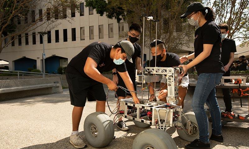 Engineering students and faculty examining a mechanical prototype