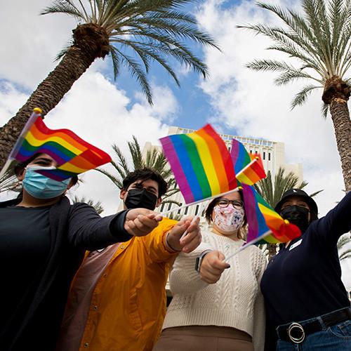 CSUF community members and students wave LGBTQ flags in front of Langsdorf Hall.